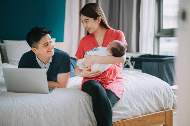 istock asian chinese father lying down on bed using laptop online shopping while mother carrying newborn baby boy in bedroom 1318884084