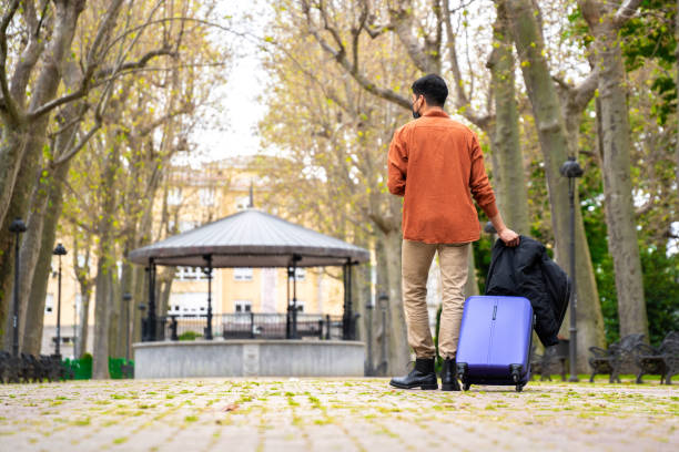 istock Latin man walking through the park with suitcase 1318884173