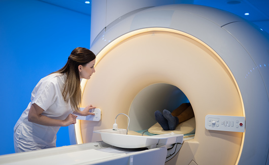 Female doctor preparing patient for scanning in MRI tunnel device. Blue illuminated room. Magnetic resonance imaging technology in specialized medical clinic.