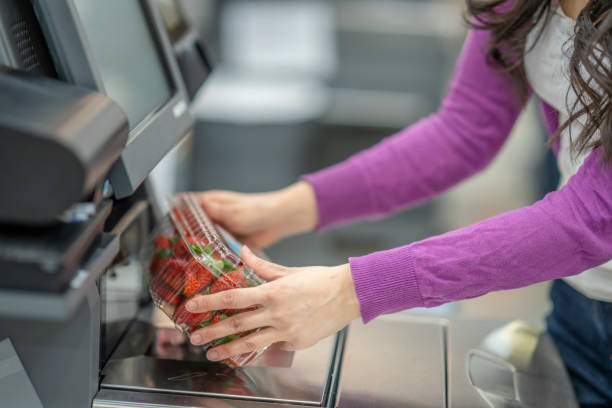 Masked Asian woman grocery shopping A middle aged woman scans a package of strawberries at a self checkout. self checkout stock pictures, royalty-free photos & images