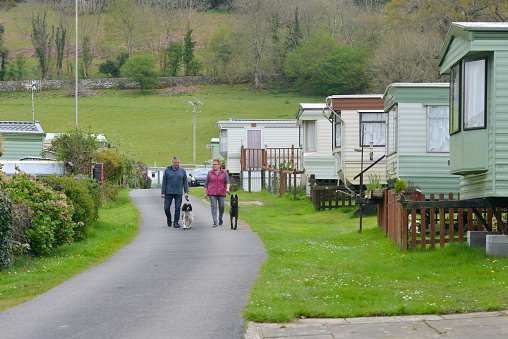 Couple walking their dogs around a caravan site with static caravans parked either side on a Spring day enjoying a vacation in rural Wales UK.