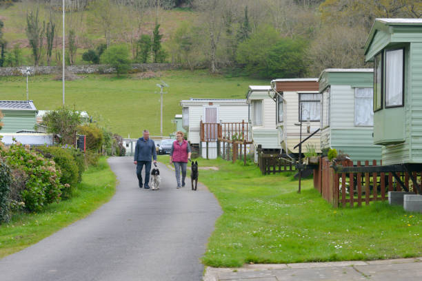 Couple walking their dogs around a caravan site with static caravans parked either side on a Spring day enjoying a vacation in rural Wales UK. stock photo