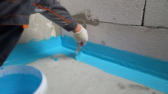 Cover the concrete wall with a cement-polymer waterproofing membrane. Waterproofing with a blue shade brush. The waterproofing coating is blue.