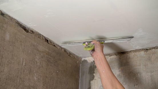 Applying putty to the ceiling with a spatula. A man puts putty on the ceiling during renovation work. Hand with a putty knife and putty, apply the mastic to the ceiling until the surface is flat.