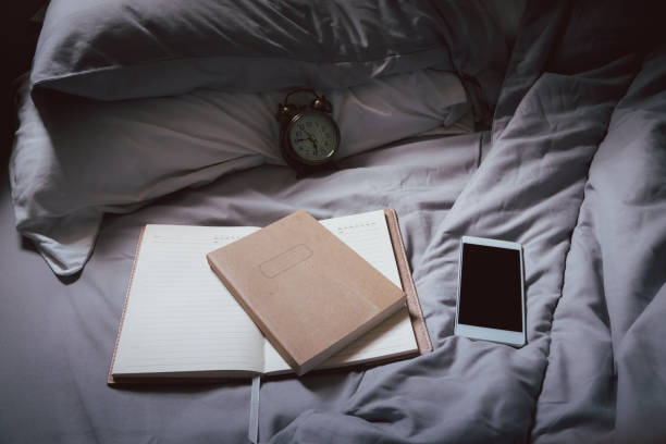 istock Diary and Planner Book on bed in bedroom. Smartphone, book with notebook and clock placed on blanket. Lifestyle of Student work at home concept. 1318894599