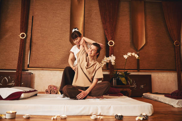 Massage therapist working on female right side Asian massage specialist lifting right arm of smiling woman while pressing her palm to client waist thai culture stock pictures, royalty-free photos & images