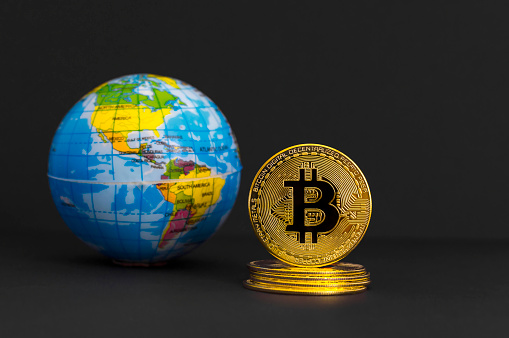 Graz, Austria-April 20, 2021: Bitcoin BTC crypto currency gold coin and Earth globe, worldwide new virtual money concept. Mining or blockchain technology