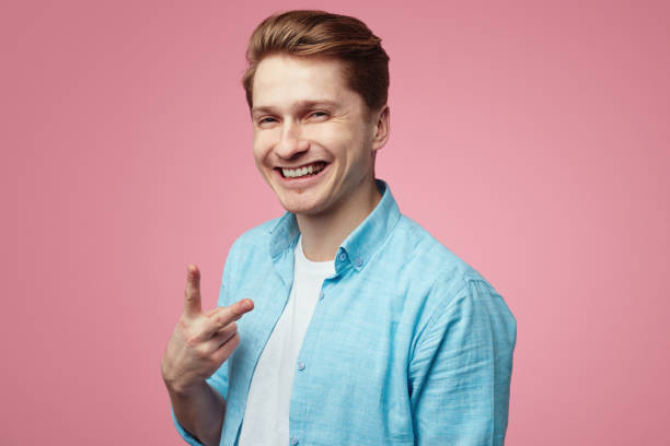 istock Smiling student wearing blue shirt and is gesturing vsign over pink wall 1318903075