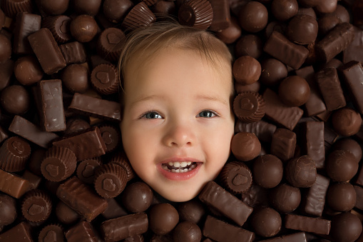 child's face close-up on a background of chocolate sweets. Excessive consumption of candy is harmful to health. Eating carbohydrates. chocolate with a heart for Valentine's Day