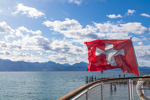 Swiss flag, set in motion by the wind, with a cloudy sky and mountains.