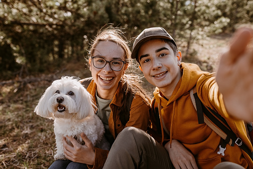 Teenage girl and boy enjoys in nature with their dog and make a selfie