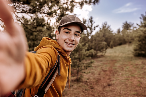 Teenage boy enjoys in nature, he is hiking in the forest and make a selfie