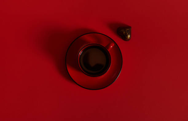 istock Flat lay composition with a red cup of coffee on a ceramic saucer and a praline in the shape of heart on red background 1318914298