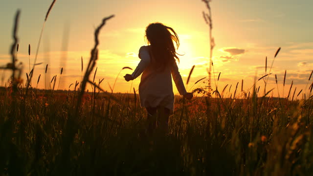 SLO MO Silhouette of a little girl running in the middle of a meadow at sunset