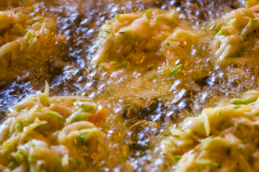 Fried vegetable fritters with zucchini, carrots, herbs, eggs, seasonings and cheese in boiling oil, close-up, selective focus