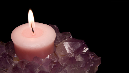Lit candle in amethyst crystal candle holder. Black background with image clipping path and text space.