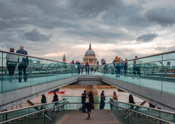 London, UK - September 4 2015: People walk on the Millennium bridge (officially known as the London Millennium Footbridge), a steel suspension bridge for pedestrians, crossing the River Thames in London, linking Bankside with the City of London. St Paul's Cathedral in the background.
