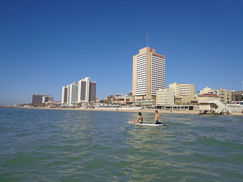 Paddle Boarders Floating on Board by Sandy Beach with the Skyline of Tel Aviv in the Background - Tel Aviv, Israel