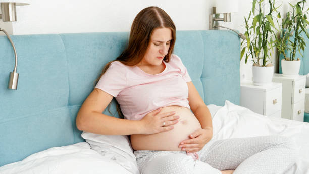 young pregnant woman feeling unwell and abdominal pain sitting on bed. healthcare and intoxication during pregnancy - intoxication imagens e fotografias de stock