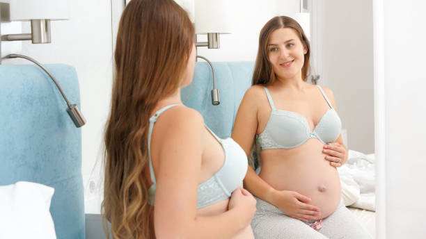 Happy smiling pregnant woman stroking her big belly and looking in reflection at mirror. Beautiful pregnancy and anticipation of baby. Happy smiling pregnant woman stroking her big belly and looking in reflection at mirror. Beautiful pregnancy and anticipation of baby  Exploring the Fetish for Expectant Mothers stock pictures, royalty-free photos & images