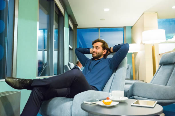 Contemplated businessman relaxing at airport lounge Smiling businessman relaxing with hands behind head on armchair. Thoughtful male professional is at airport lounge. He is on business trip. airport departure area stock pictures, royalty-free photos & images
