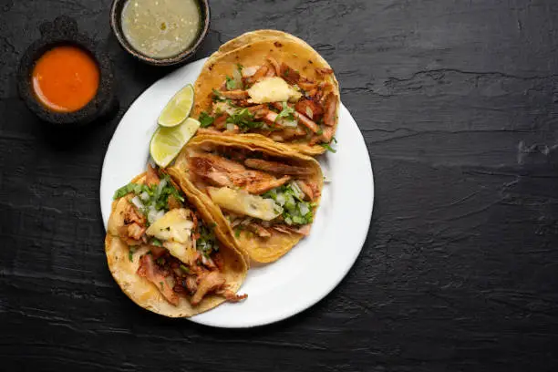 Pork tacos called al pastor with pineapple on dark background. Traditional mexican tacos