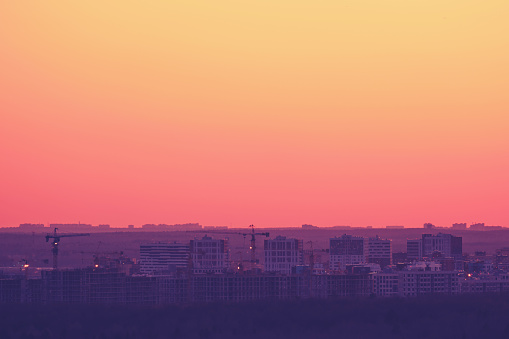 Background of bright red sky and building houses with tower cranes