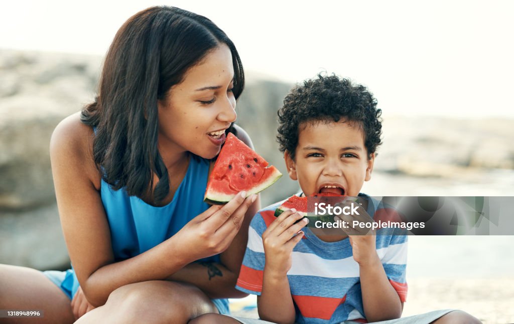 Shot of a mother and sitting down and enjoying some watermelon at the beach Watermelon is out favourite fruit Summer Stock Photo