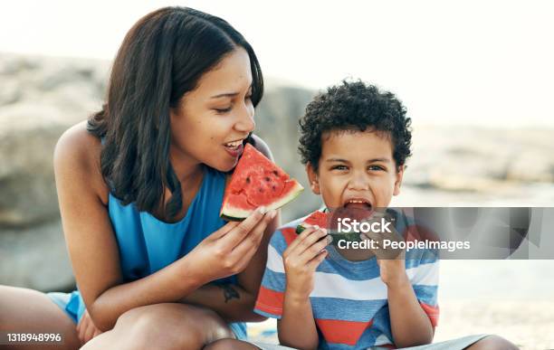 Shot Of A Mother And Sitting Down And Enjoying Some Watermelon At The Beach Stock Photo - Download Image Now