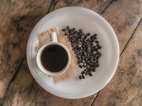 Cup with coffee on a white plate accompanied by artisan roasted coffee beans, on top of a rustic wooden table, ready to enjoy, produced in Guatemala.