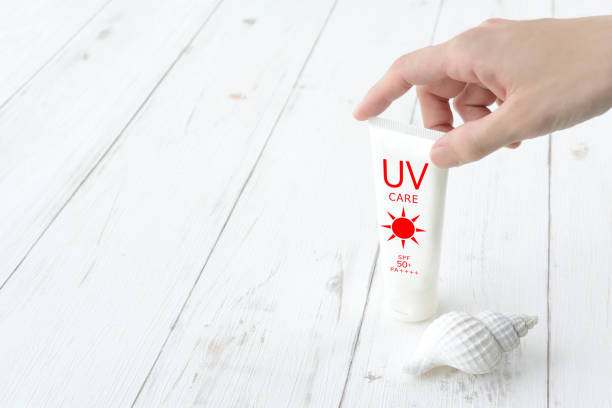 Woman' hand picking sunscreen cream and shell on white wooden board
