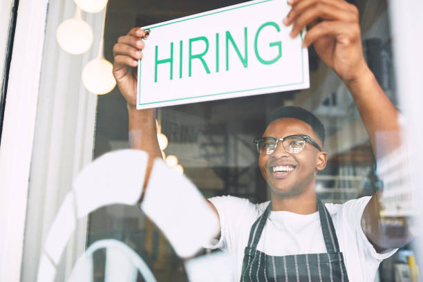 Shot of a young man hanging up a hiring sign while working in a cafe A growing business needs a growing team help wanted sign photos stock pictures, royalty-free photos & images
