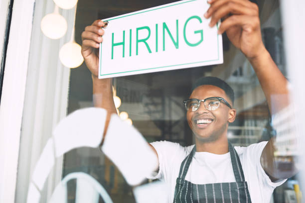 shot of a young man hanging up a hiring sign while working in a cafe - help wanted sign imagens e fotografias de stock