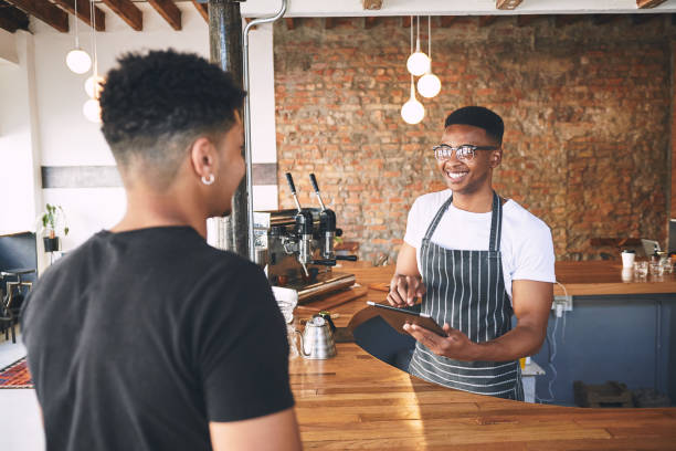 istock Shot of a young man using a digital tablet while serving a customer in a cafe 1318951845