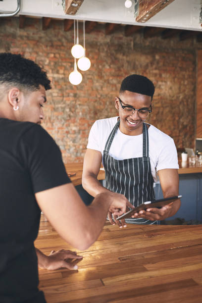 istock Shot of a young man using a digital tablet while serving a customer in a cafe 1318951846
