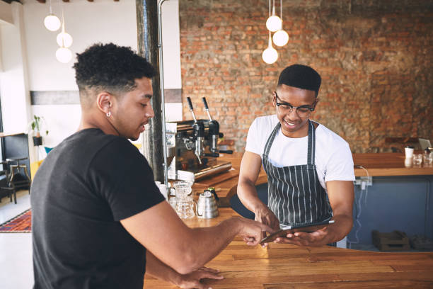 istock Shot of a young man using a digital tablet while serving a customer in a cafe 1318951848