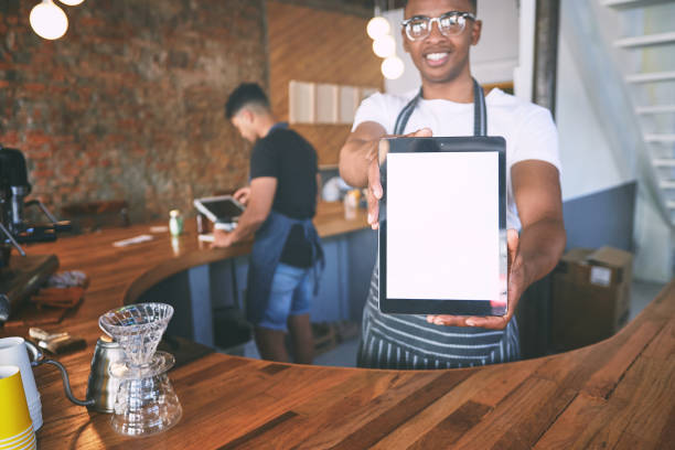 Shot of a young man showing a digital tablet with a blank screen while working in a cafe