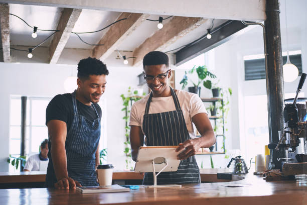 Shot of two young men using a digital tablet while working in a cafe The smart tech that keeps their sales up point of sale stock pictures, royalty-free photos & images