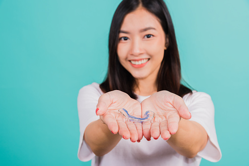 Portrait young Asian beautiful woman smiling holding silicone orthodontic retainers for teeth on hand palm, Teeth retaining tools after removable braces, Orthodontics dental healthy care concept