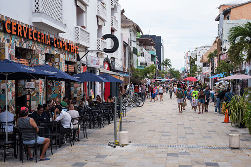 Playa del Carmen, Mexico - May 17, 2021: Tourists, some wearing masks because of the Covid-19 pandemic, walk along the popular three-mile long pedestrian stretch of 5th Avenue, or Quinta Avenida, in Playa del Carmen.