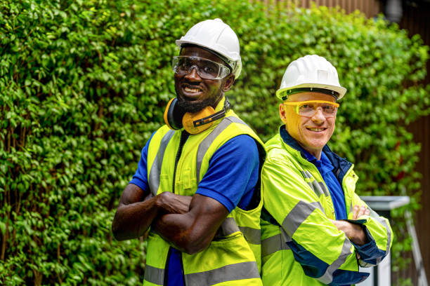 istock team factory worker technician engineer men standing confidence with green working suite dress and safety helmet. Background of green trees wall. 1318964246