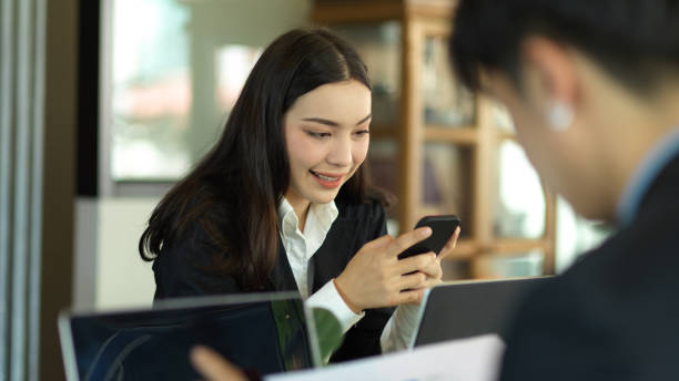 istock Businesswoman smiling and using smartphone while working with coworker 1318965037