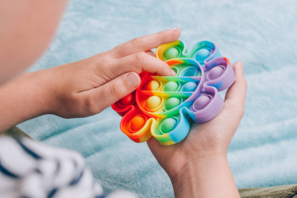 мальчик играет с радугой поп это непоседа игрушка. нажмите пузырь ерзать сенсорной игрушкой - моютые и многоразовые кремния стресс-помощь и - distracted стоковые фото и изображения