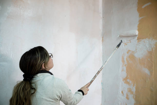istock a woman using a roller with white paint to paint the wall 1318969990