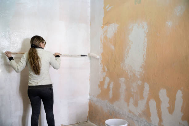 istock a young woman using a roller with white paint to paint the wall 1318969994