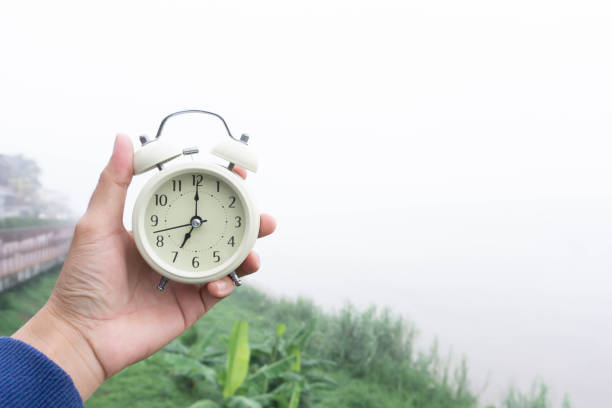 despertador en mano con naturaleza y fondo de niebla por la mañana - daylight savings fotografías e imágenes de stock