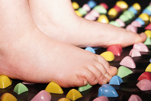 Massage mat with colorful stones for the foot. Child feet standing doing foot massage on a massage Mat for Flatfoot Treatment. Child healthcare concept. Selective focus.