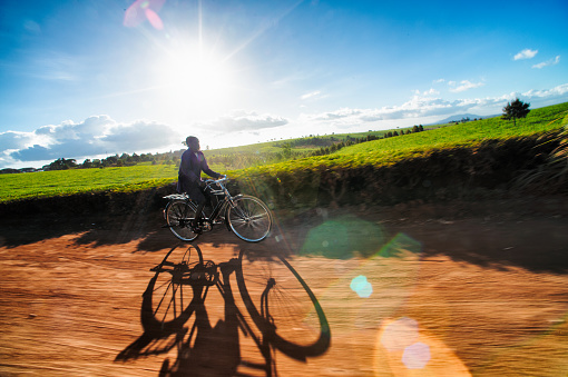 Back lit African Adult Male on a transport bicycle cycling on a dirt road in motion between tea plantations with lens flare close to Mount Mulanje Southern Malawi Africa