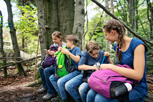 Family hiking in the forest. They are sitting on the bench on the trail and having some snack and water.\nPolish mountains Gorce.\nNikon D850