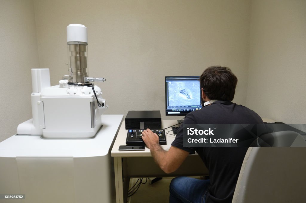 Young man scientist working with scanning electron microscope. Laboratory technician observing samples with a SEM. Electron Microscope Stock Photo